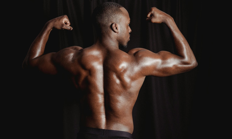 Homem negro de costas e tronco nu, com boxers pretos e braços no ar, evidenciando seus músculos e pensando sobre o que e fio terra no sexo.